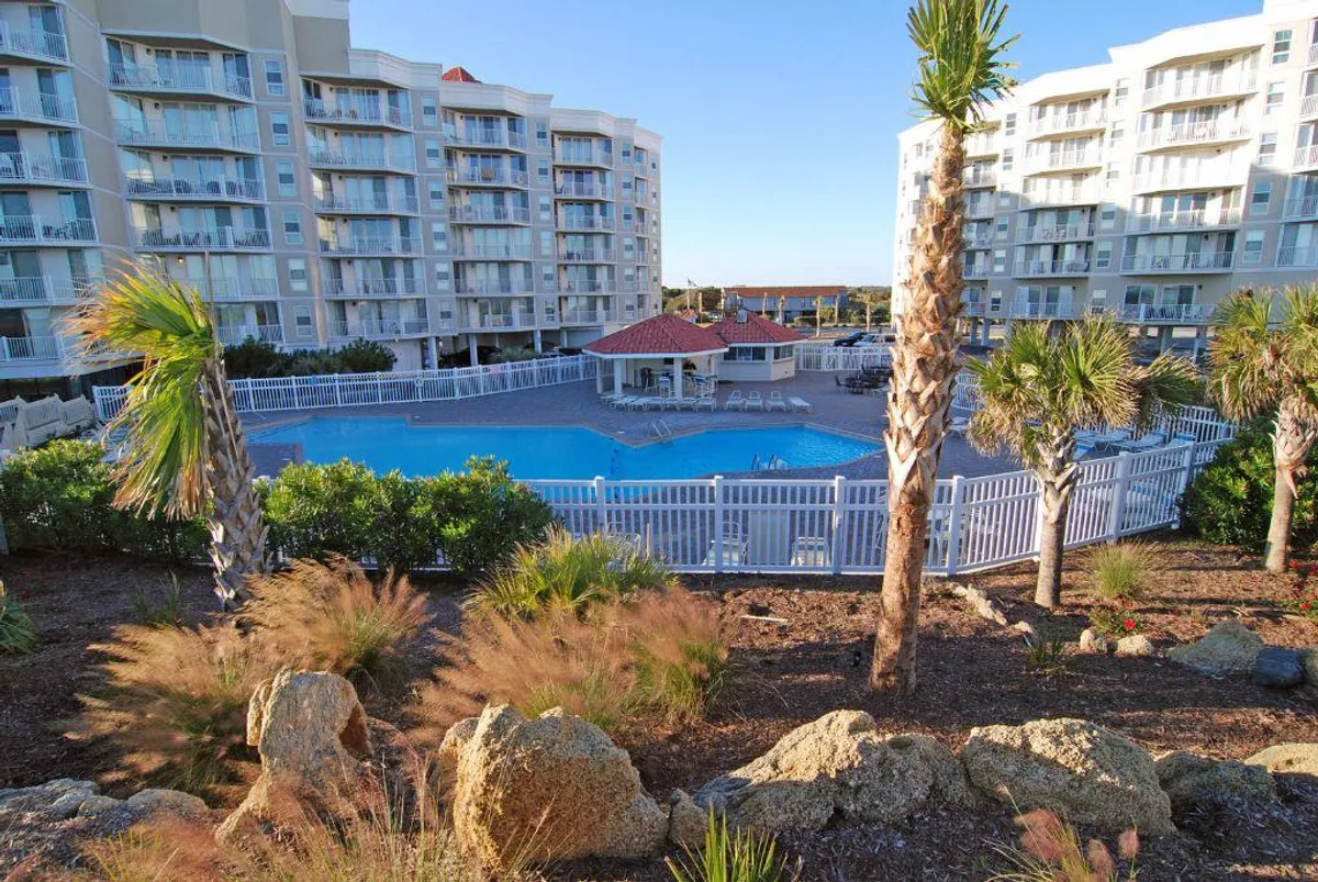 This image features a sparkling swimming pool surrounded by palm trees, with benches and resort buildings in the background. The inviting blue water, greenery, and poolside seating create a sense of leisure and relaxation, central to the resort lifestyle.