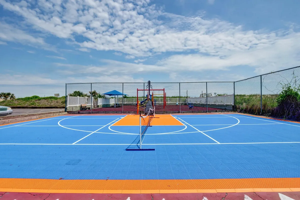 A vibrant, brightly colored sports court outfitted for basketball and tennis, surrounded by greenery. This outdoor activity area highlights the resort's recreational amenities available just steps away from the living spaces.