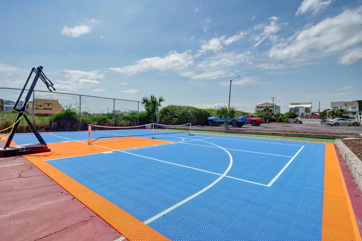 A dynamic view of an outdoor sports court featuring a basketball hoop, tennis net, and lush greenery surrounding the area. The environment is vibrant and inviting, perfect for friendly competitions and active recreation.