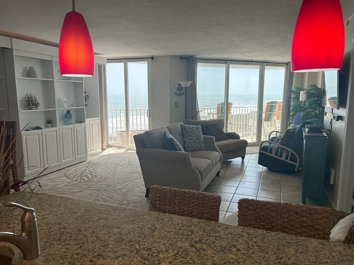 Featuring a comfortable sofa oriented towards large windows that frame an inspiring ocean view, this living area is accented with decorative elements on shelves, contributing to a tranquil and welcoming atmosphere. Natural light streams in, inviting quiet moments or social gatherings.