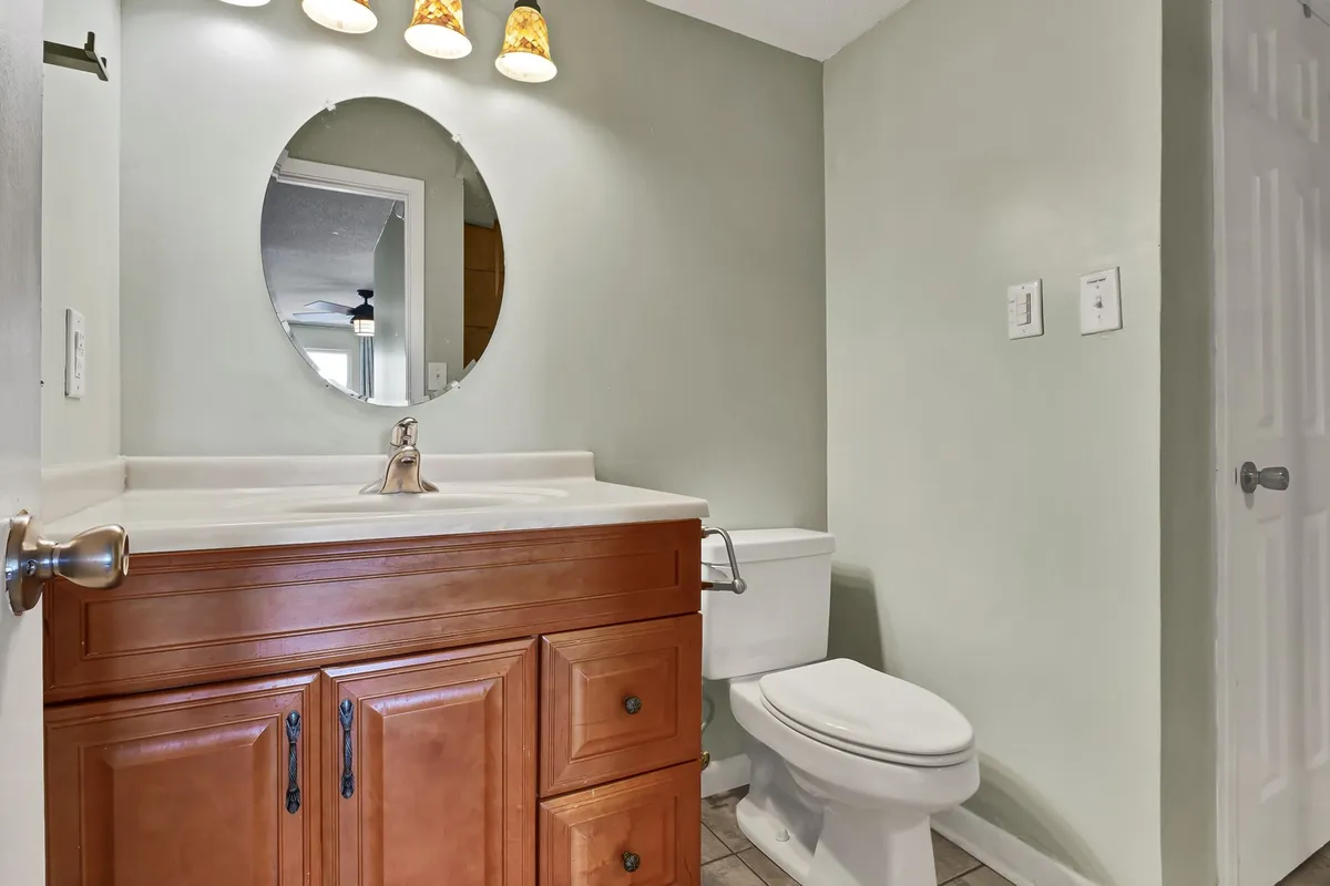 A stylish bathroom vanity with a wooden cabinet, round mirror, and elegant light fixtures. Sunlight reflects gently off the mirror, creating a fresh, inviting atmosphere ideal for self-care and winding down.