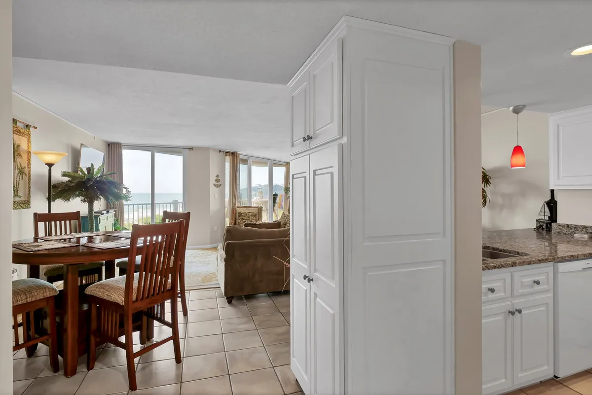 This image showcases an open-concept living and dining area with a cozy dining table, a comfortable sofa, inviting kitchen cabinetry, and large windows that allow abundant natural light to fill the space. The overall ambiance is warm and welcoming, perfect for both relaxing and socializing.